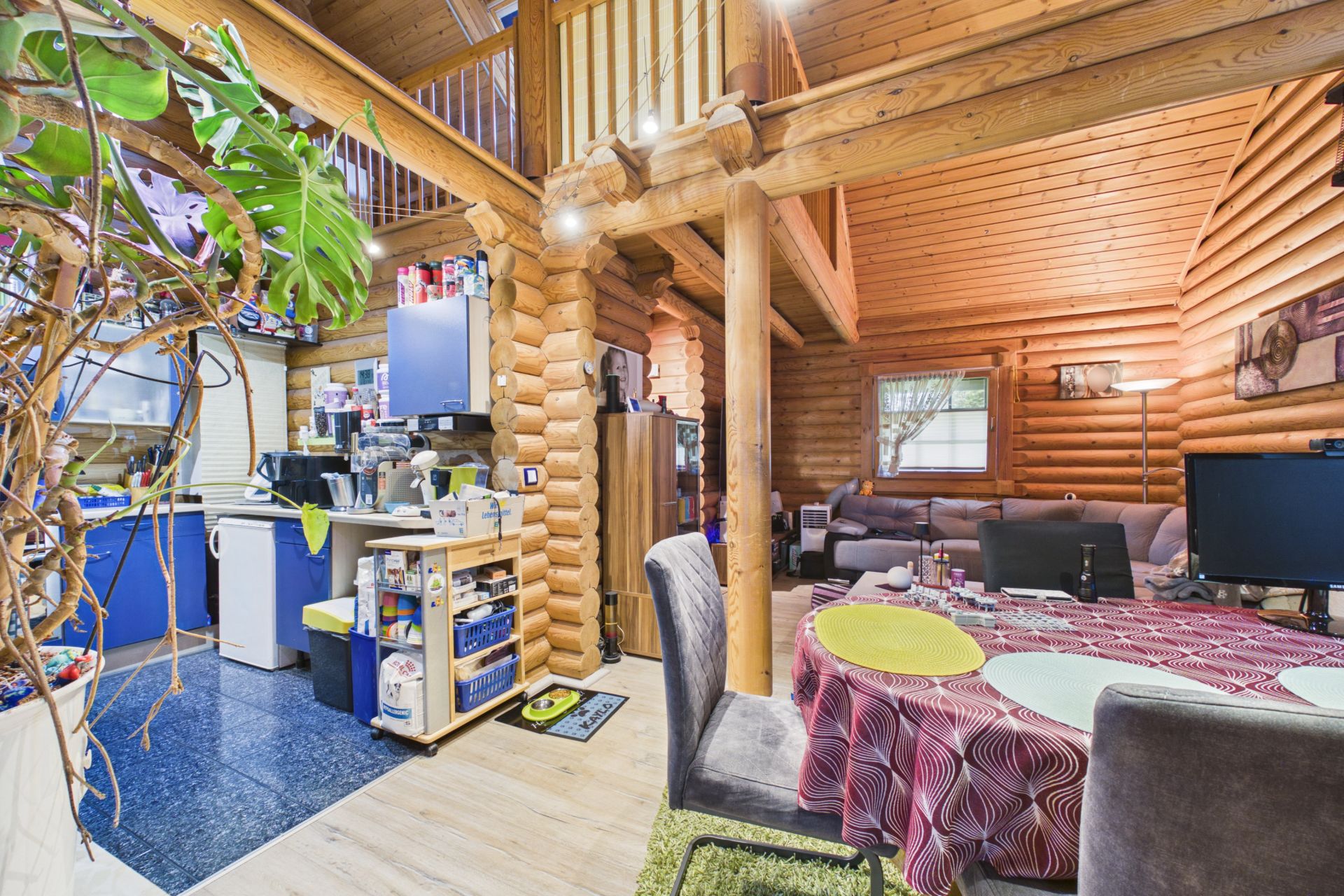 Wohnbereich in einem Holzhaus mit Essecke, Küche und Wohnzimmer mit Sofa und Fernseher.