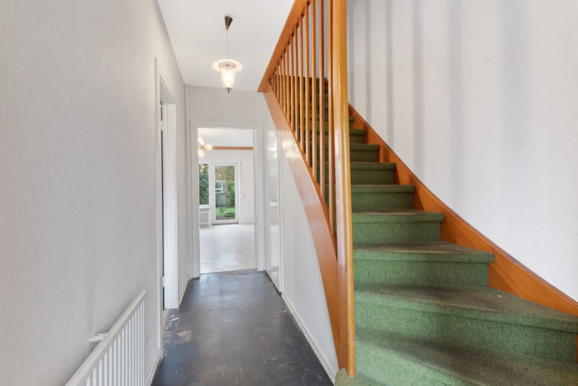 Flur mit grünem Teppichtreppe, weißer Wand und Blick ins Wohnzimmer mit Garten.