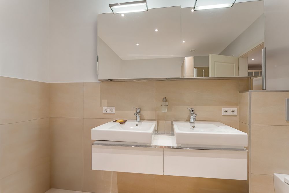 Modernes Badezimmer mit zwei Waschbecken, Spiegel und hellen Fliesen.