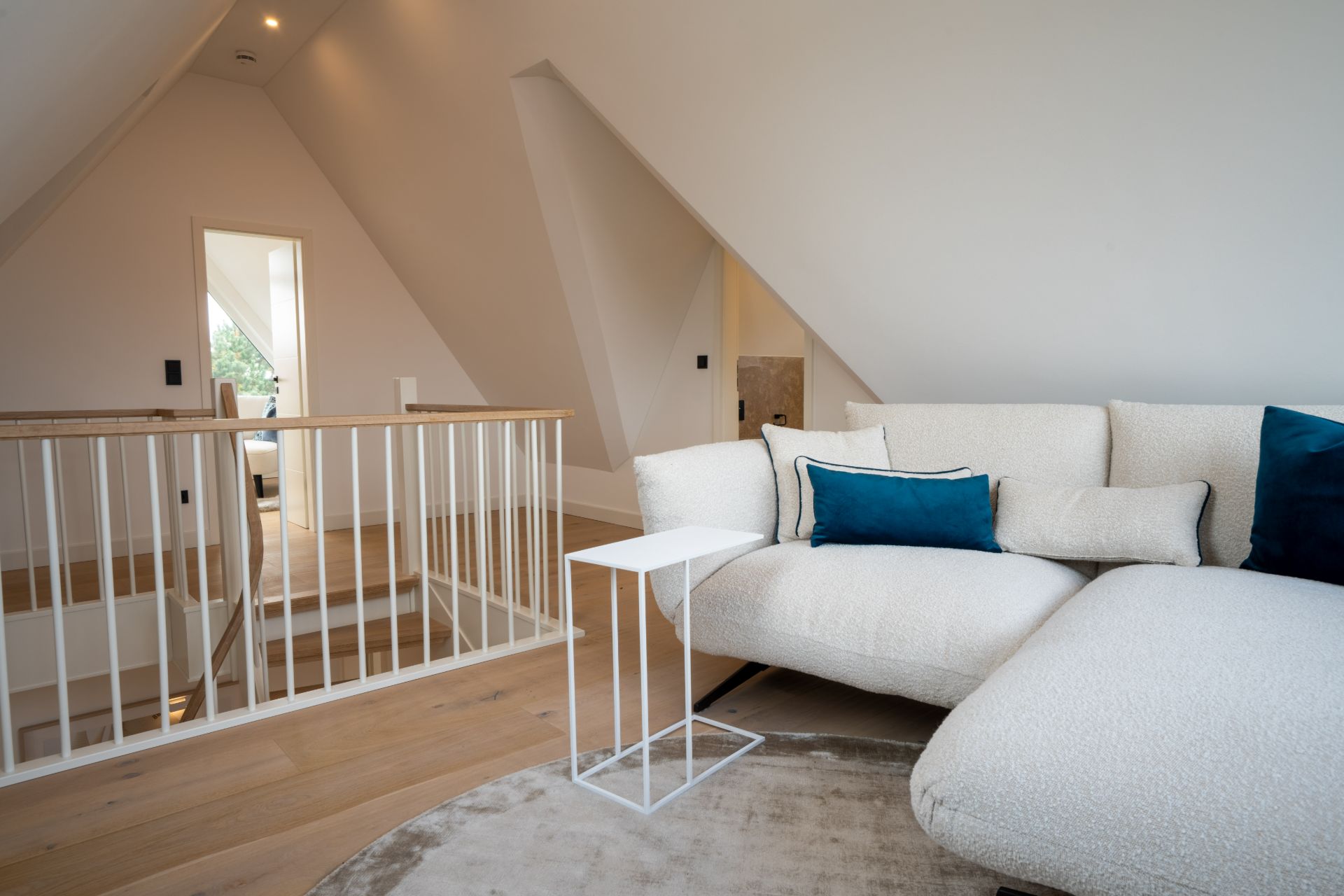Modernes Wohnzimmer auf einer Dachgeschoss-Etage mit Sofa, kleinem Tisch und Holztreppe mit Geländer.