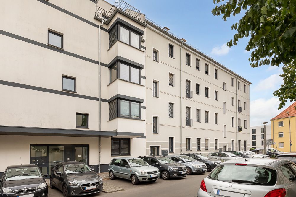 Mehrstöckiges Wohngebäude mit parkenden Autos davor an einer Straße.
