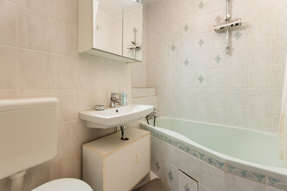 Kleines Badezimmer mit Badewanne, Waschbecken, Spiegel und Toilette, alles in hellen Fliesen gehalten.