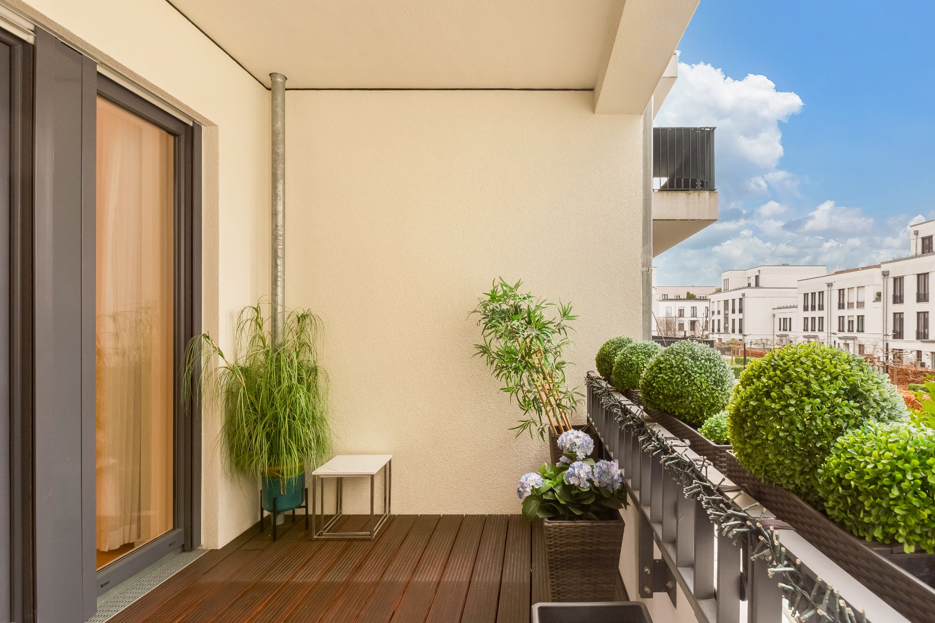 Moderner Balkon mit Holzfußboden, Topfpflanzen und Ausblick auf Wohngebäude.
