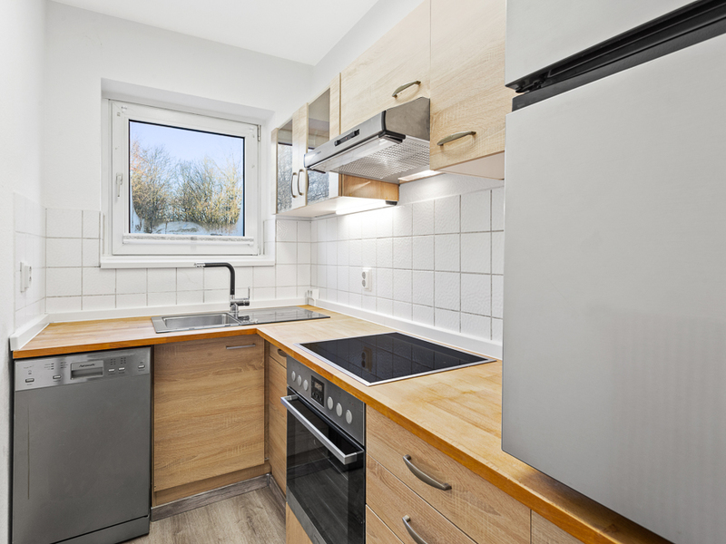 Moderne Einbauküche mit Holzarbeitsplatte, Ceranfeld, Spüle, Geschirrspüler und Fenster.