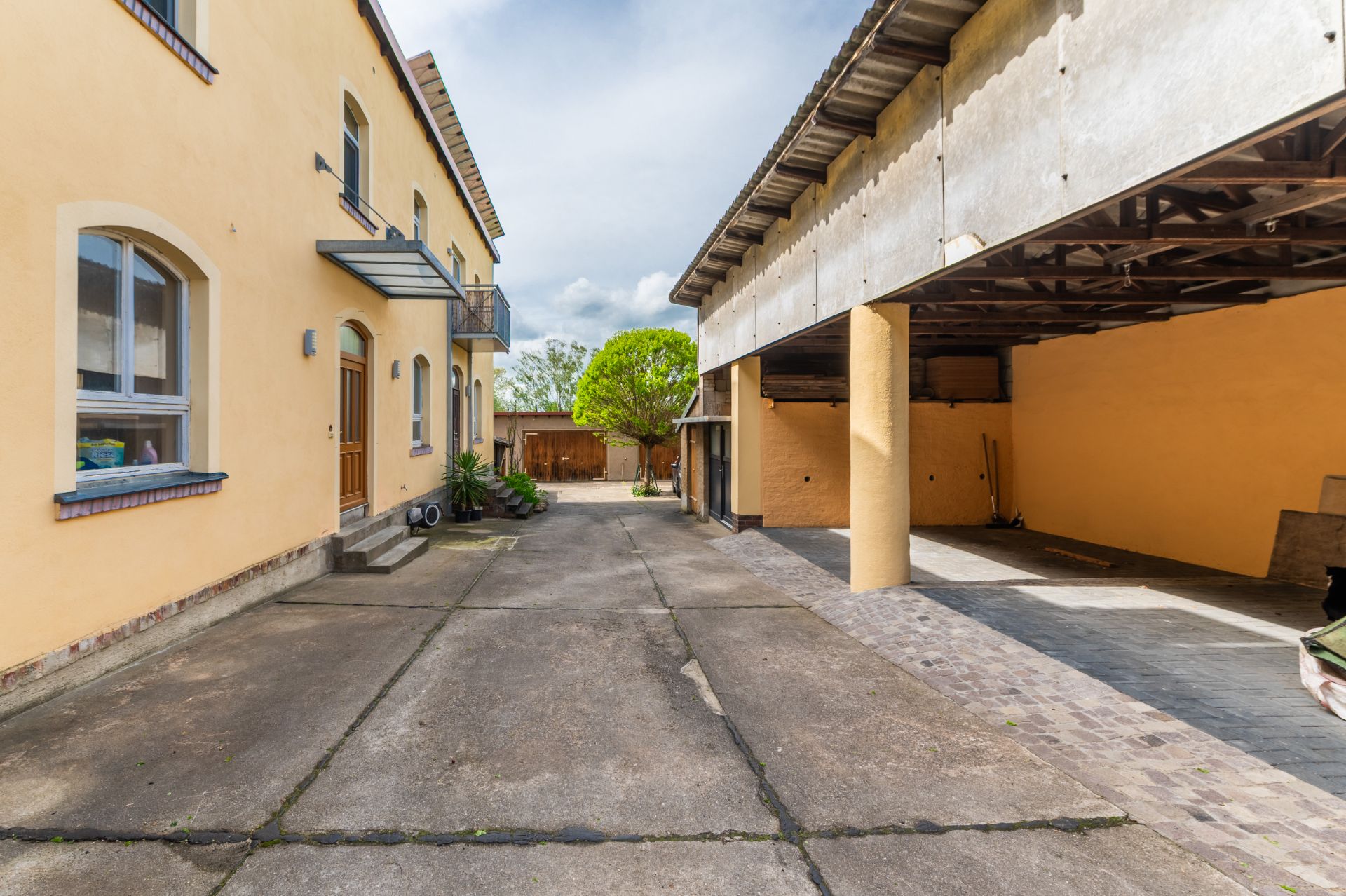Gepflasterter Innenhof mit gelbem Wohngebäude links und überdachtem Bereich rechts.