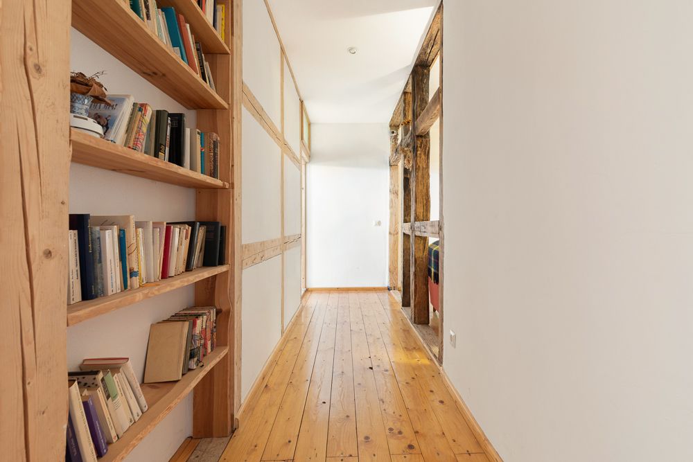 Heller Flur mit Bücherregal aus Holz und offenem Zugang zu einem weiteren Raum.