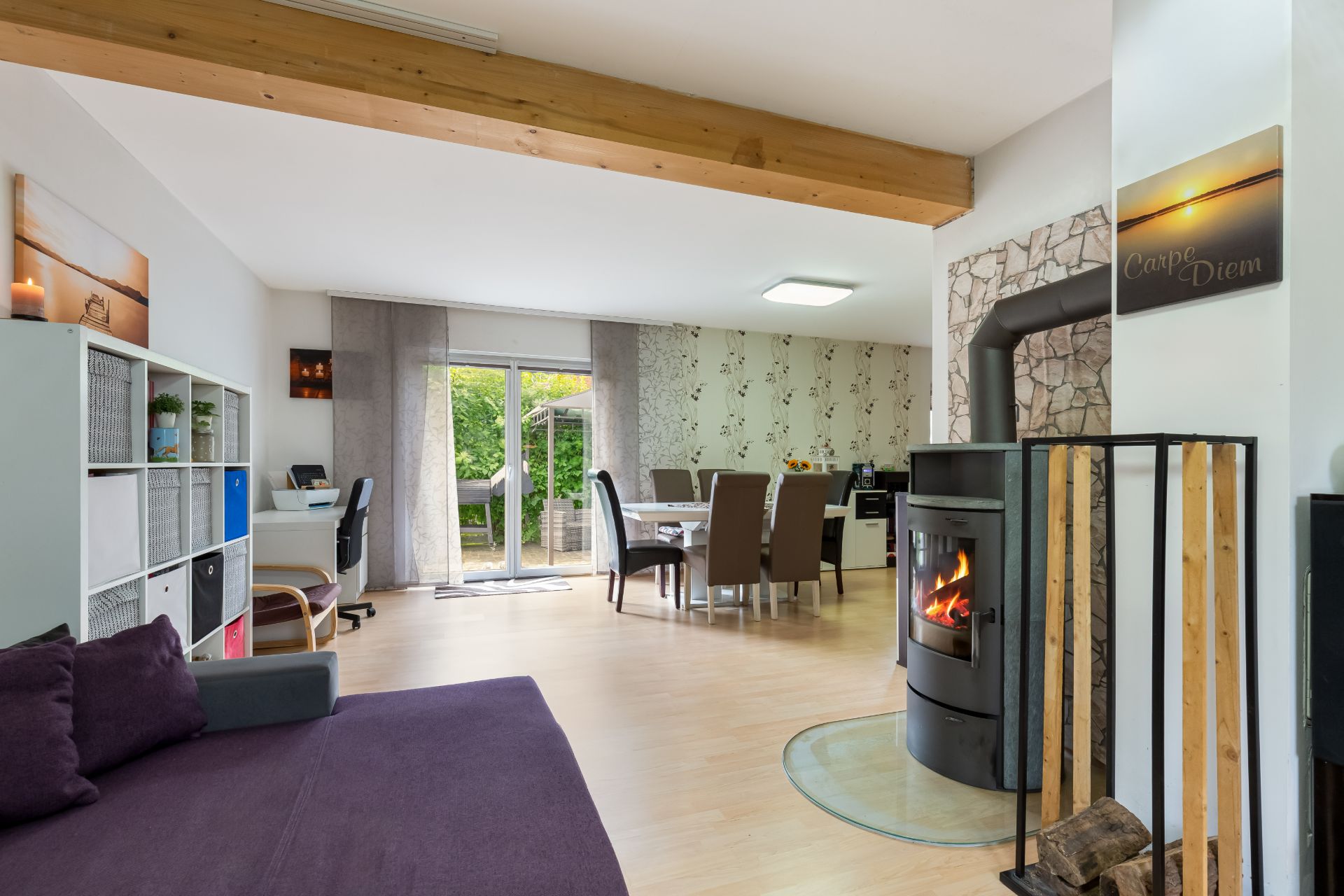 Helles Wohnzimmer mit Kamin, Esstisch, Sofa und großem Fenster zum Garten.