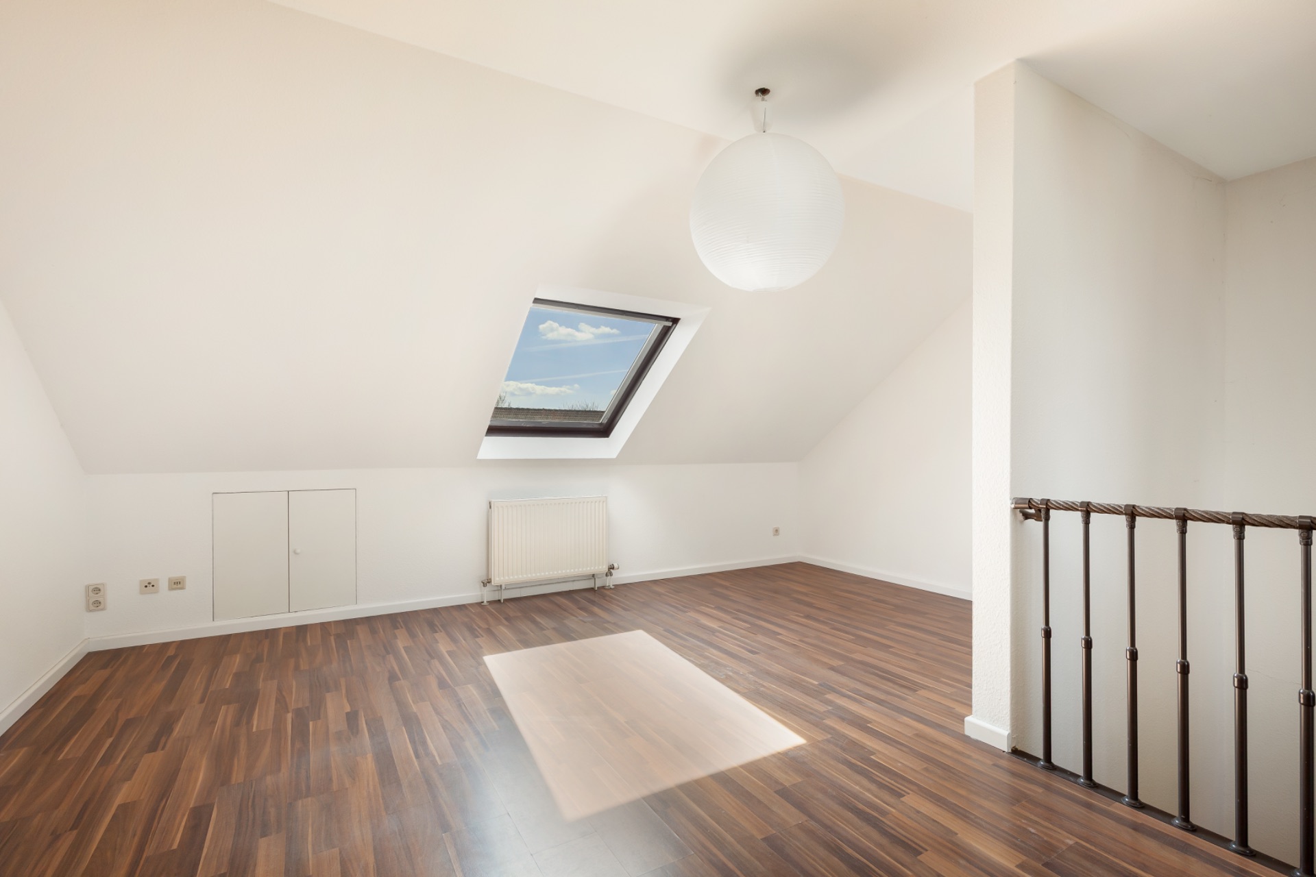 Heller Dachgeschossraum mit Dachfenster, Holzfußboden und weißer Wand.