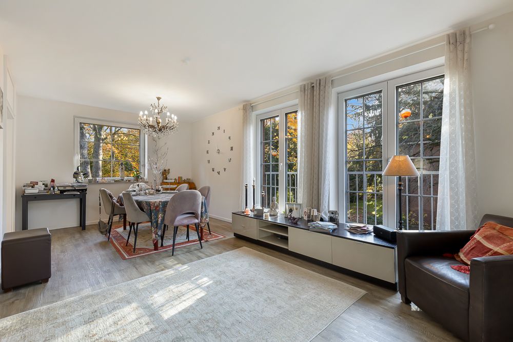 Helles Wohnzimmer mit Esstisch, Stühlen, Sofa, großen Fenstern und Blick auf den Garten.