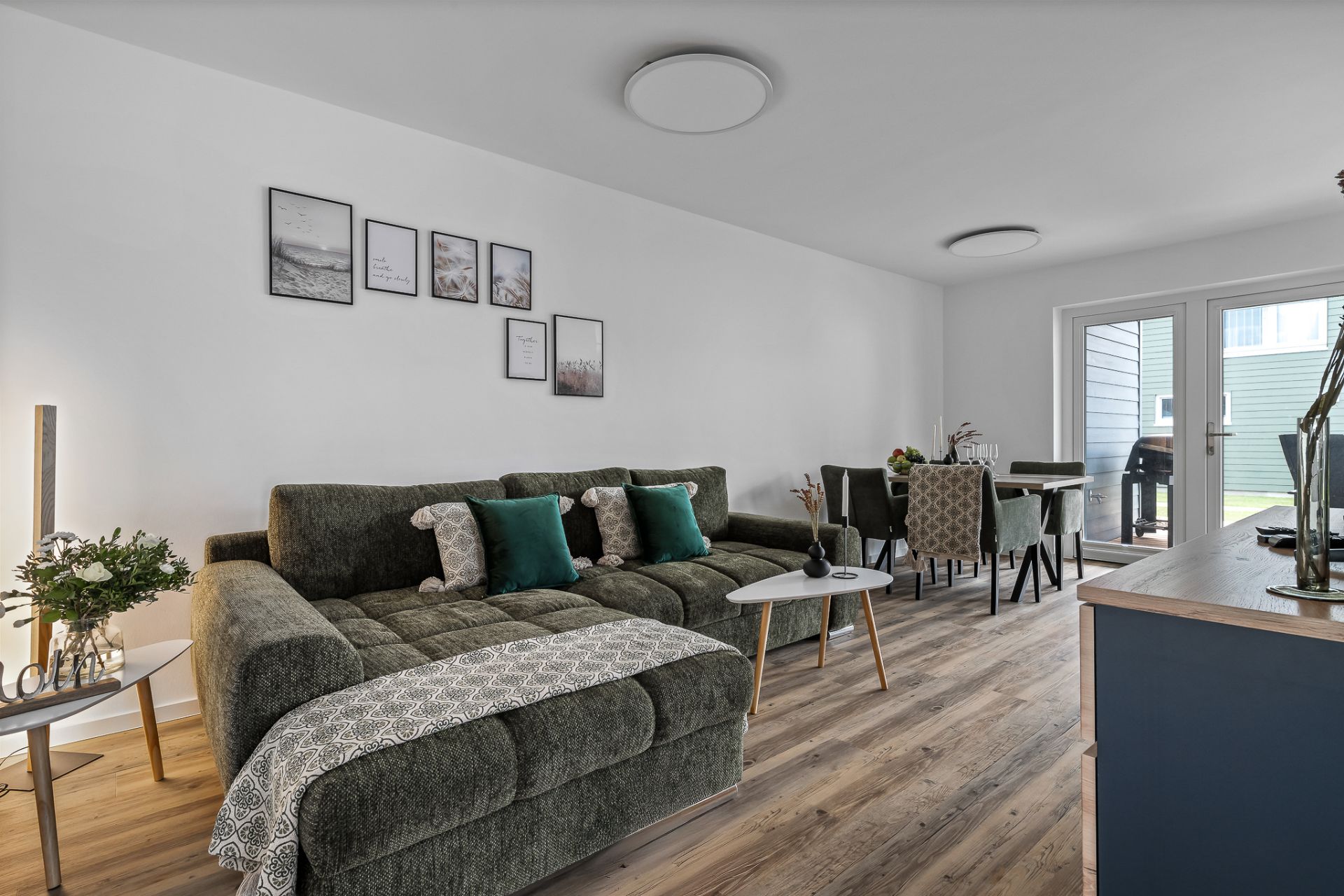 Modernes Wohnzimmer mit grünem Sofa, Esstisch und Zugang zur Terrasse.