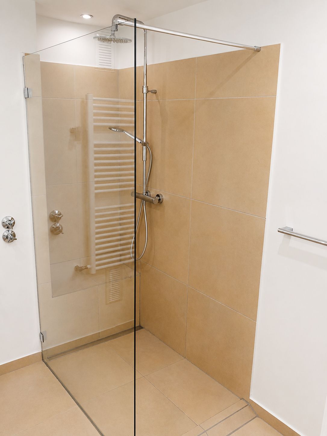 Moderne, offene Dusche mit Glaswand, beigen Fliesen und Handtuchheizkörper.
