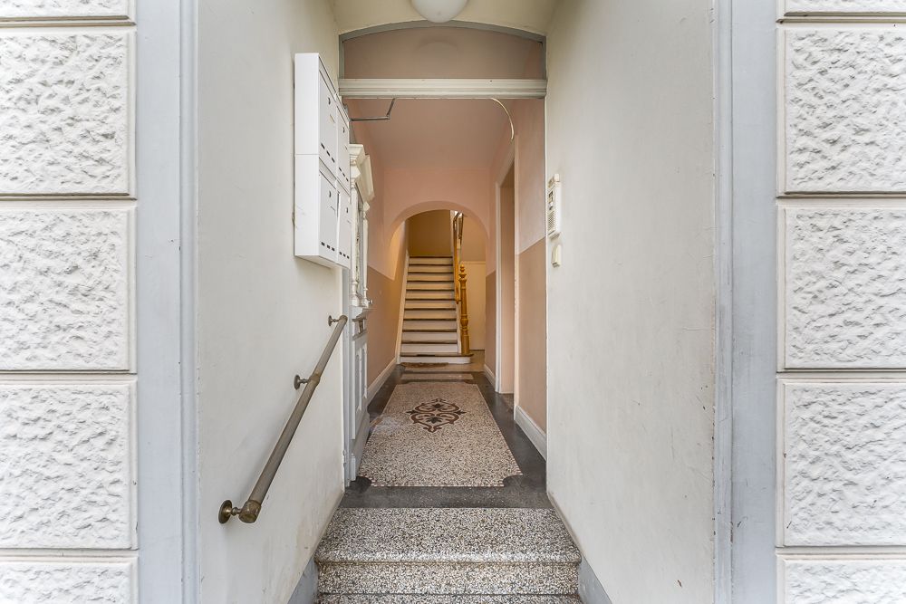 Blick in einen Hausflur mit Briefkästen, Geländer und Treppe im Hintergrund.