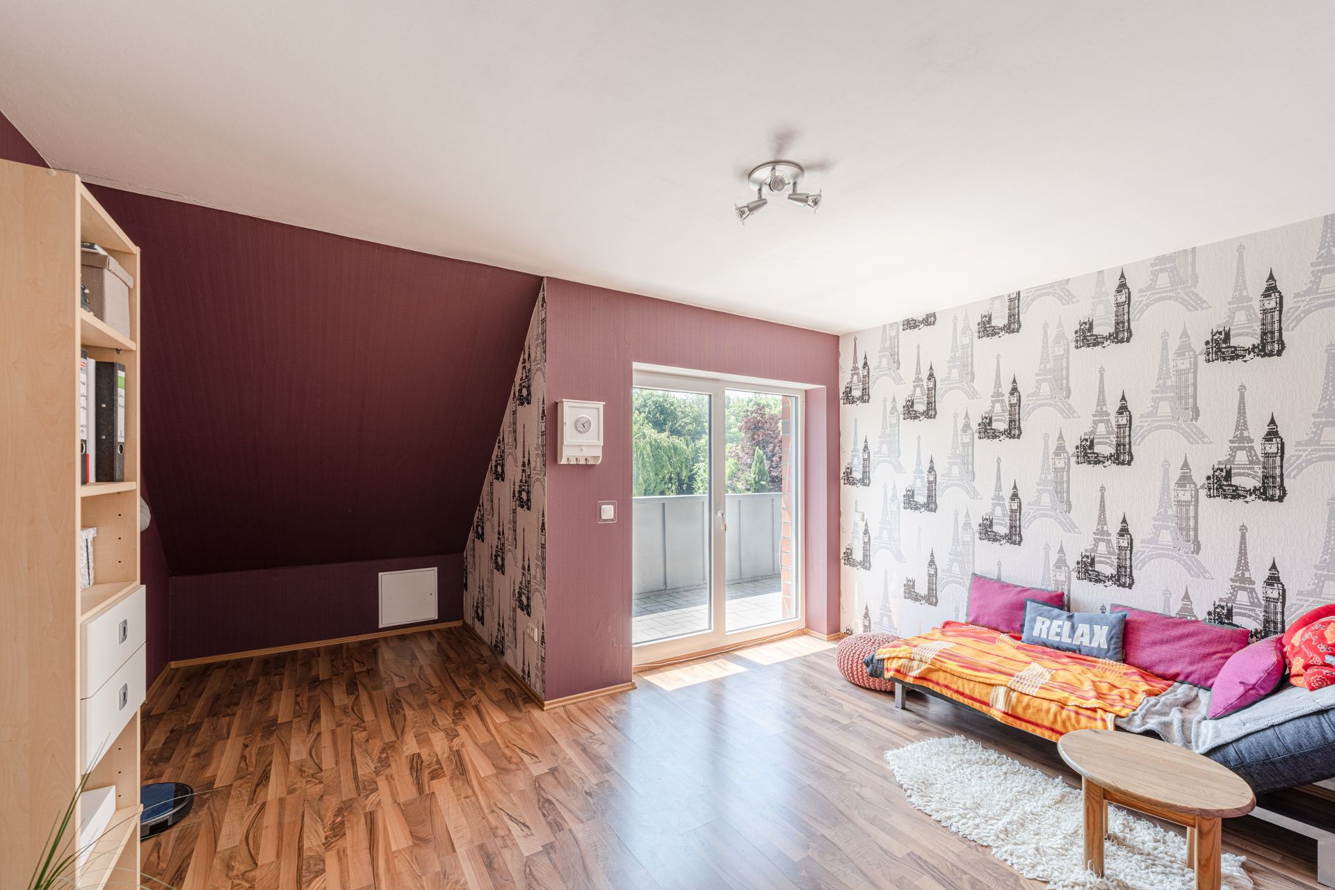 Helles Wohnzimmer mit Holzfußboden, Sofa, kleinem Tisch und Zugang zum Balkon.