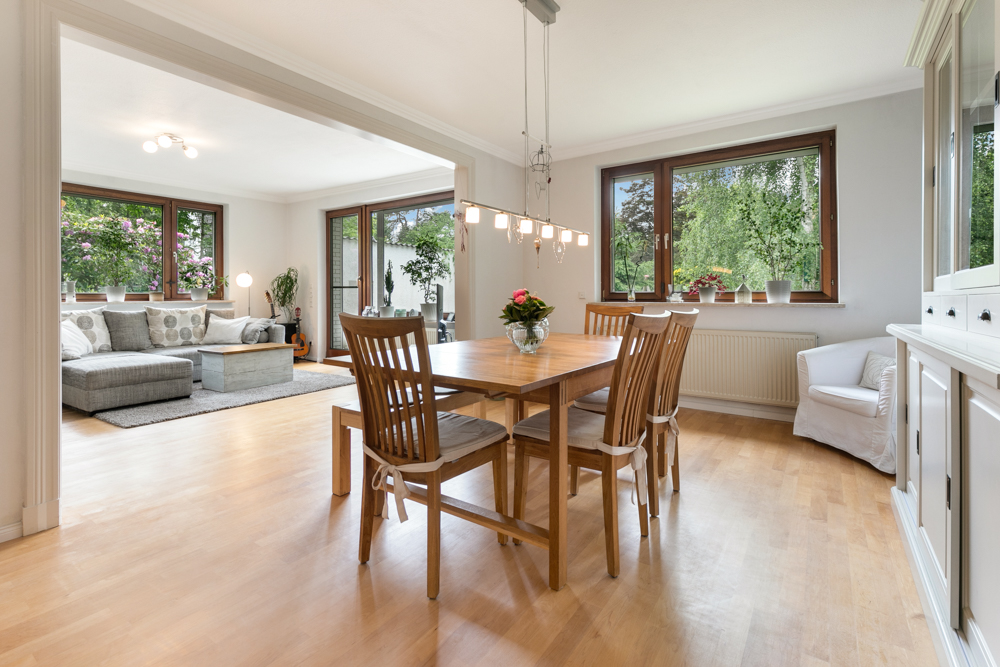 Heller Essbereich mit Holztisch und sechs Stühlen, angrenzend an Wohnzimmer mit Sofa.