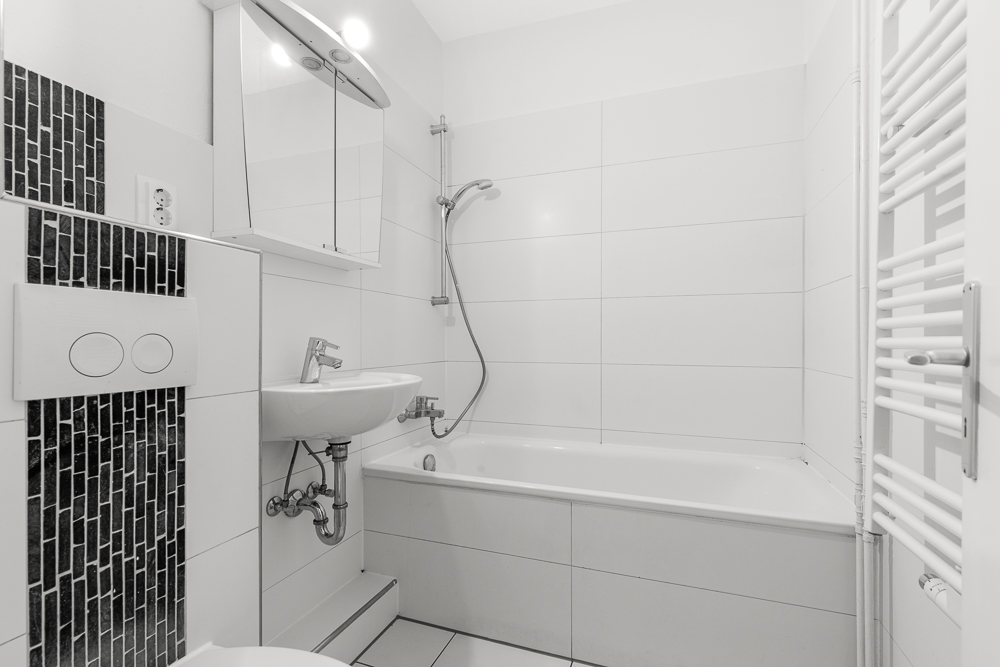 Helles Badezimmer mit Badewanne, Waschbecken, Spiegel und Handtuchheizkörper.