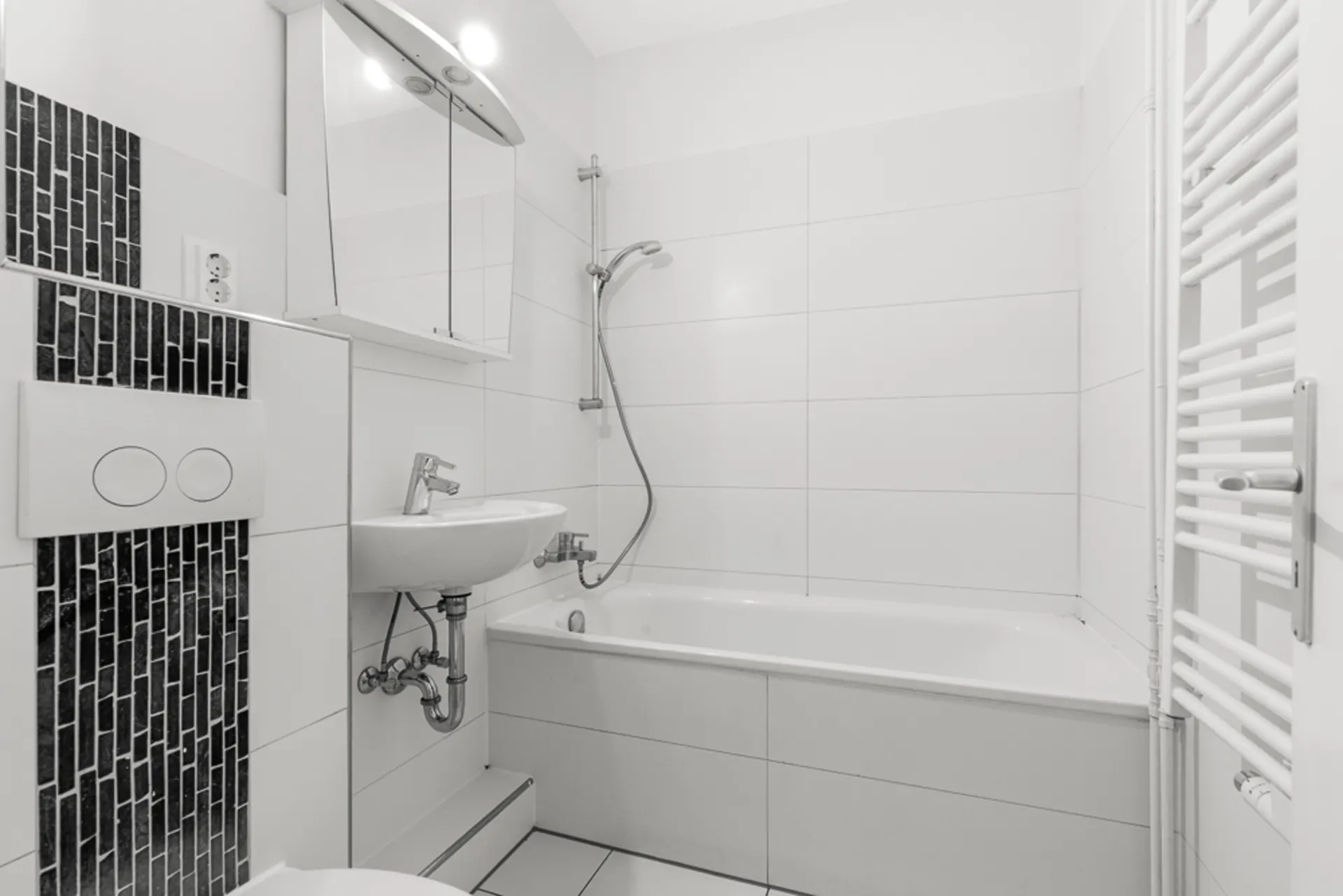 Helles Badezimmer mit Badewanne, Waschbecken, Spiegel und Handtuchheizkörper.