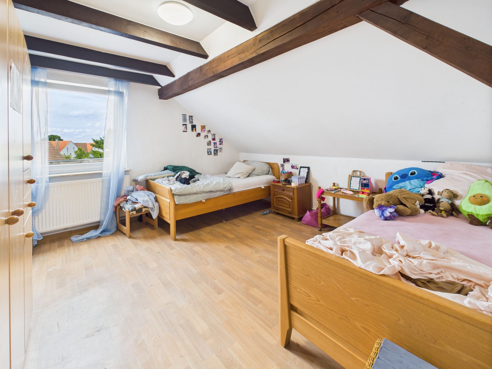 Helles Schlafzimmer mit zwei Einzelbetten, Holzboden und sichtbaren Deckenbalken.
