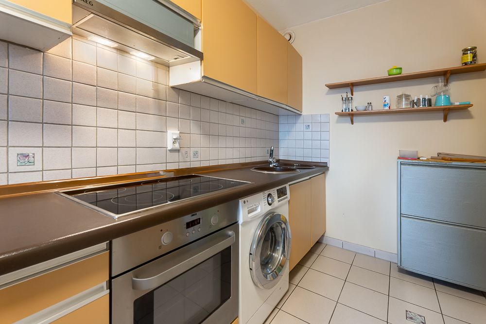 Kleine Küche mit Herd, Ofen, Waschmaschine, Spüle und Regalen an der Wand.