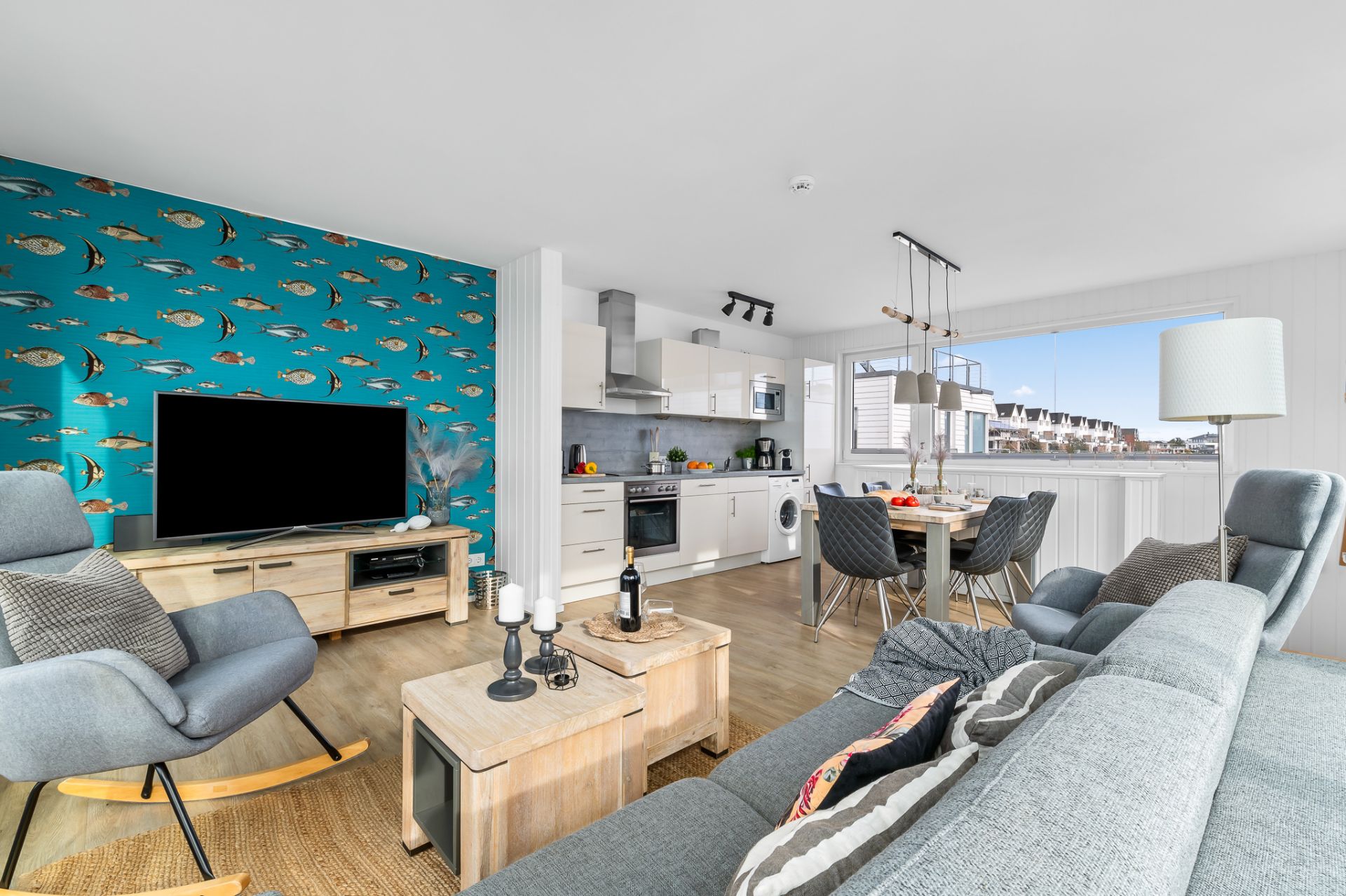 Modernes Wohnzimmer mit Küchenbereich, Esstisch und auffälliger Tapete mit Fischen.