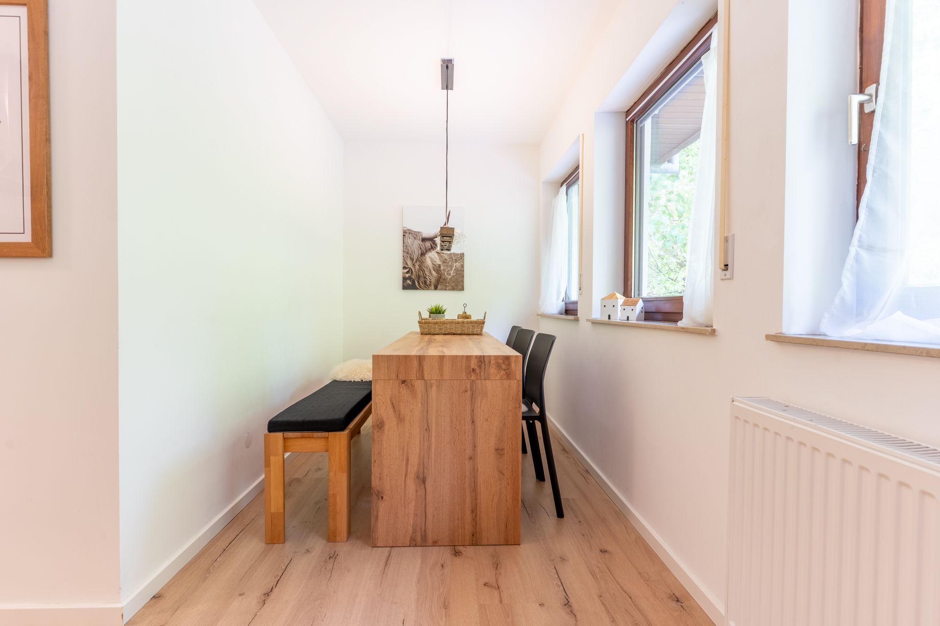 Heller Essbereich mit Holztisch, Bank und zwei Stühlen an Fenstern.
