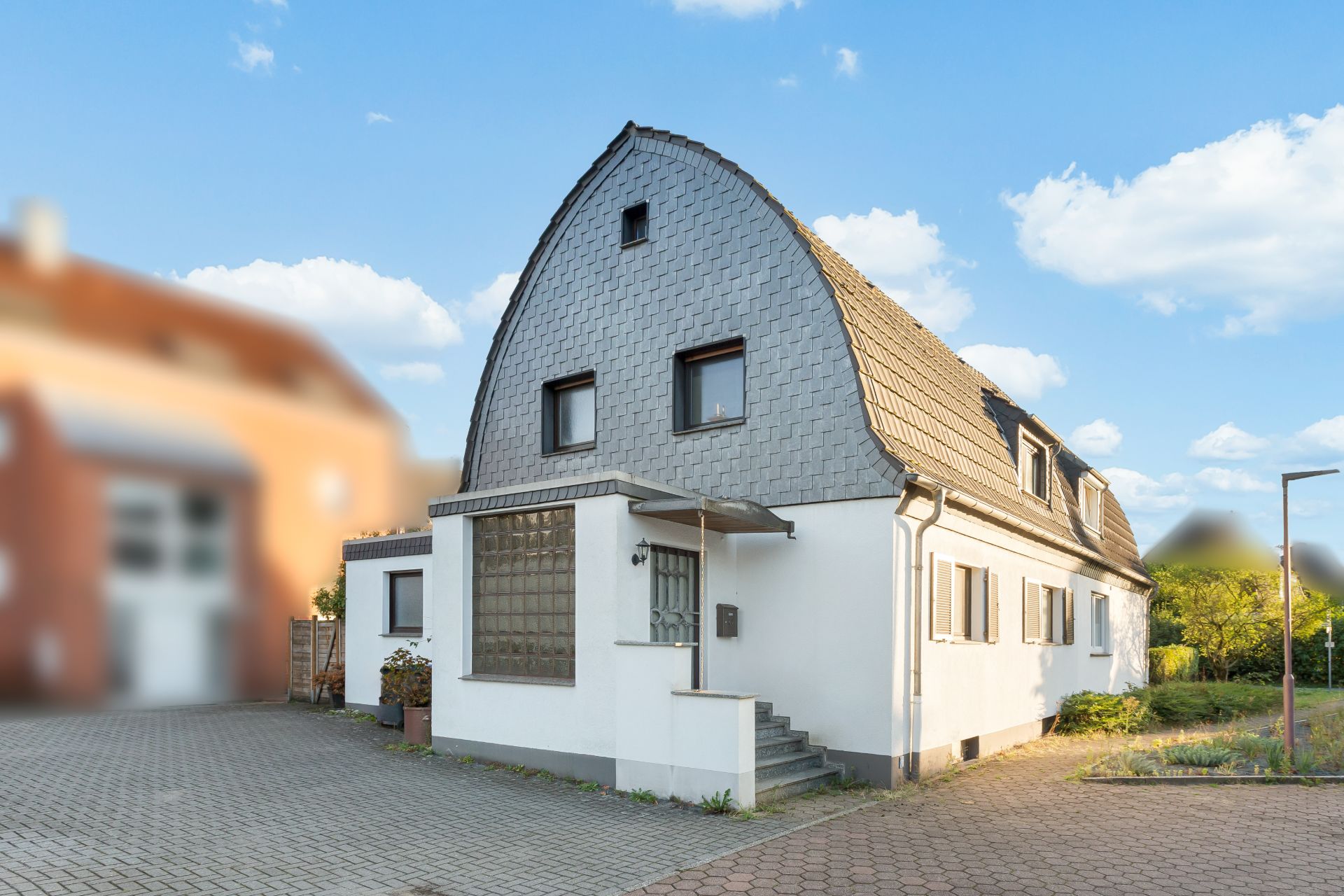 Weißes Einfamilienhaus mit geschwungenem Dach und Pflastersteinen im Vordergrund.