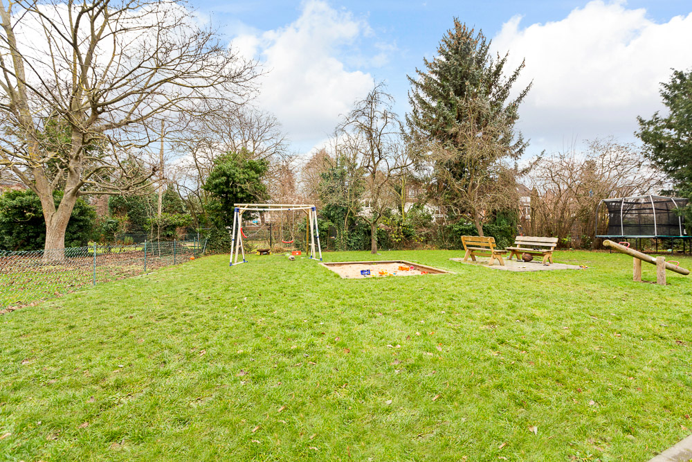 Grüner Garten mit Schaukel, Sandkasten, Holzbänken und Trampolin.