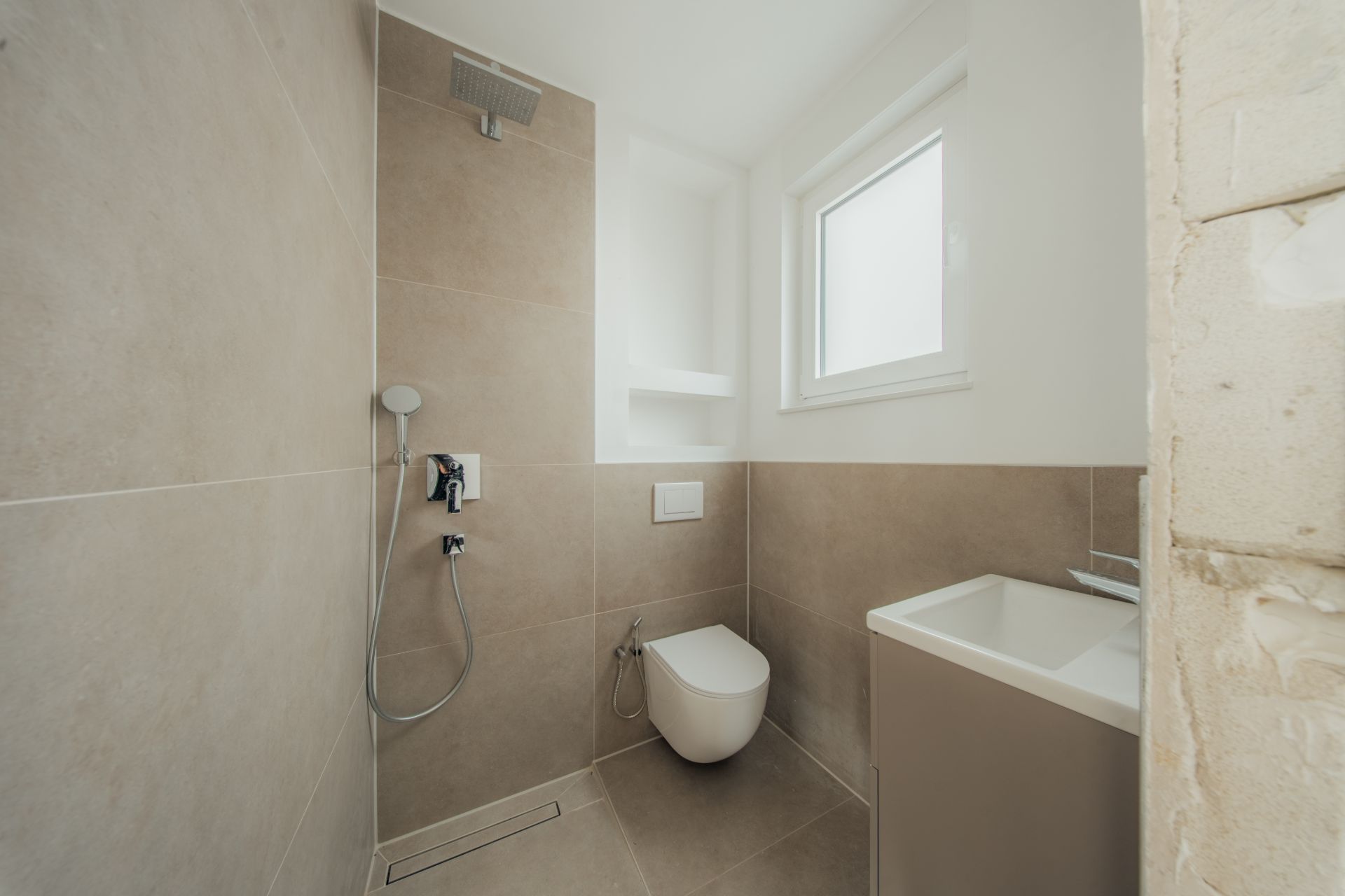Modernes Badezimmer mit ebenerdiger Dusche, Wand-WC, Waschbecken und Fenster.