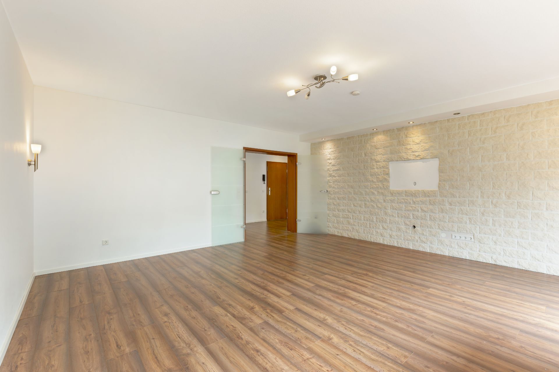 Leeres Wohnzimmer mit Holzfußboden und heller Steinwand.
