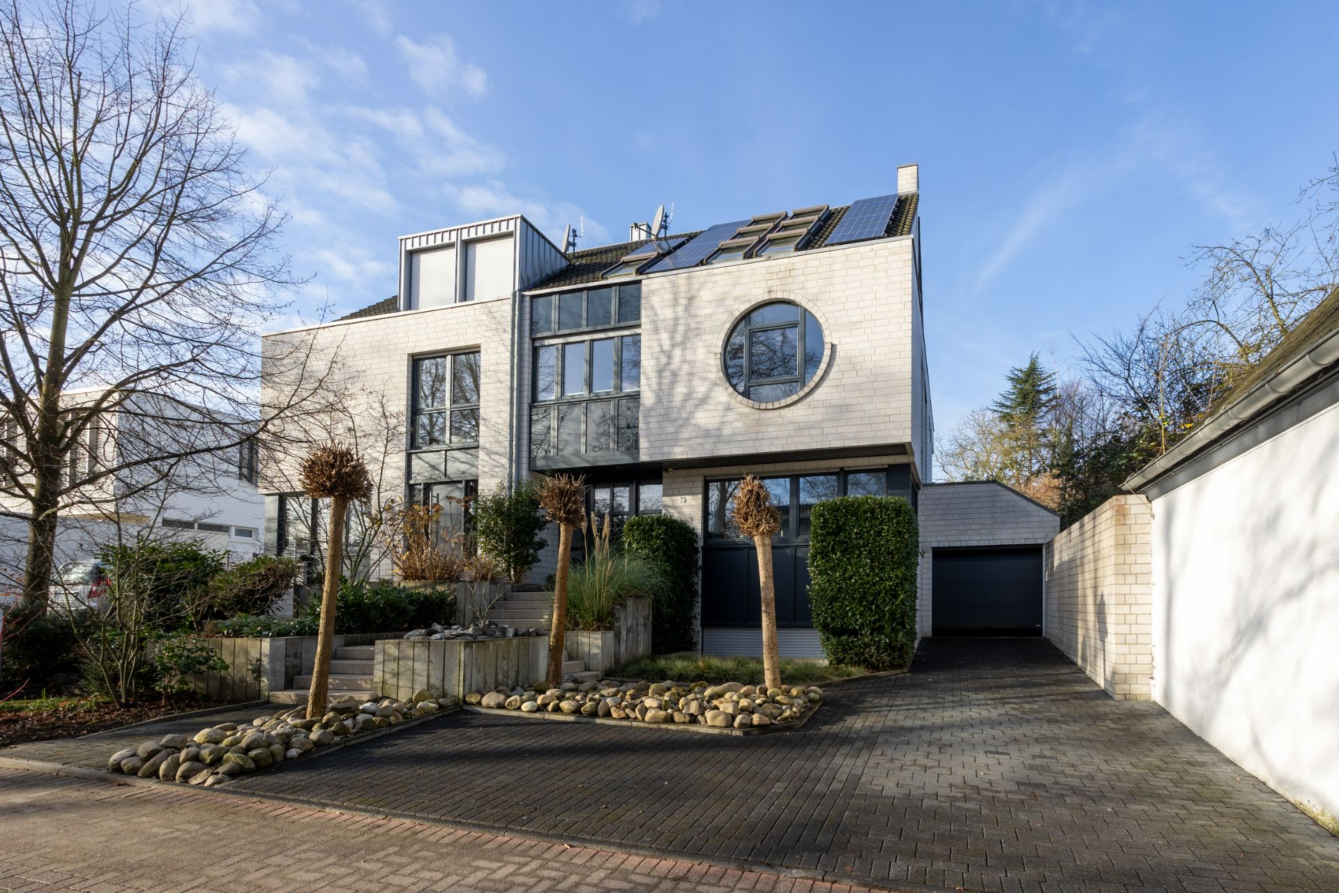 Modernes Wohnhaus mit großen Fenstern, runder Fensterfront und gepflasterter Einfahrt.
