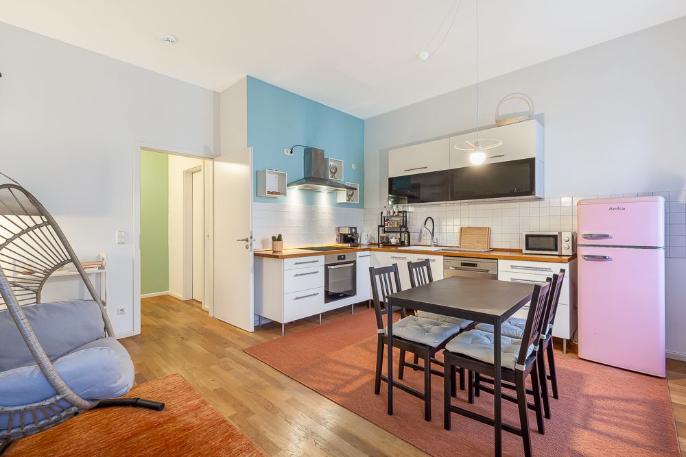 Moderne Wohnküche mit Esstisch, Stühlen, pinkem Kühlschrank und Hängesessel.