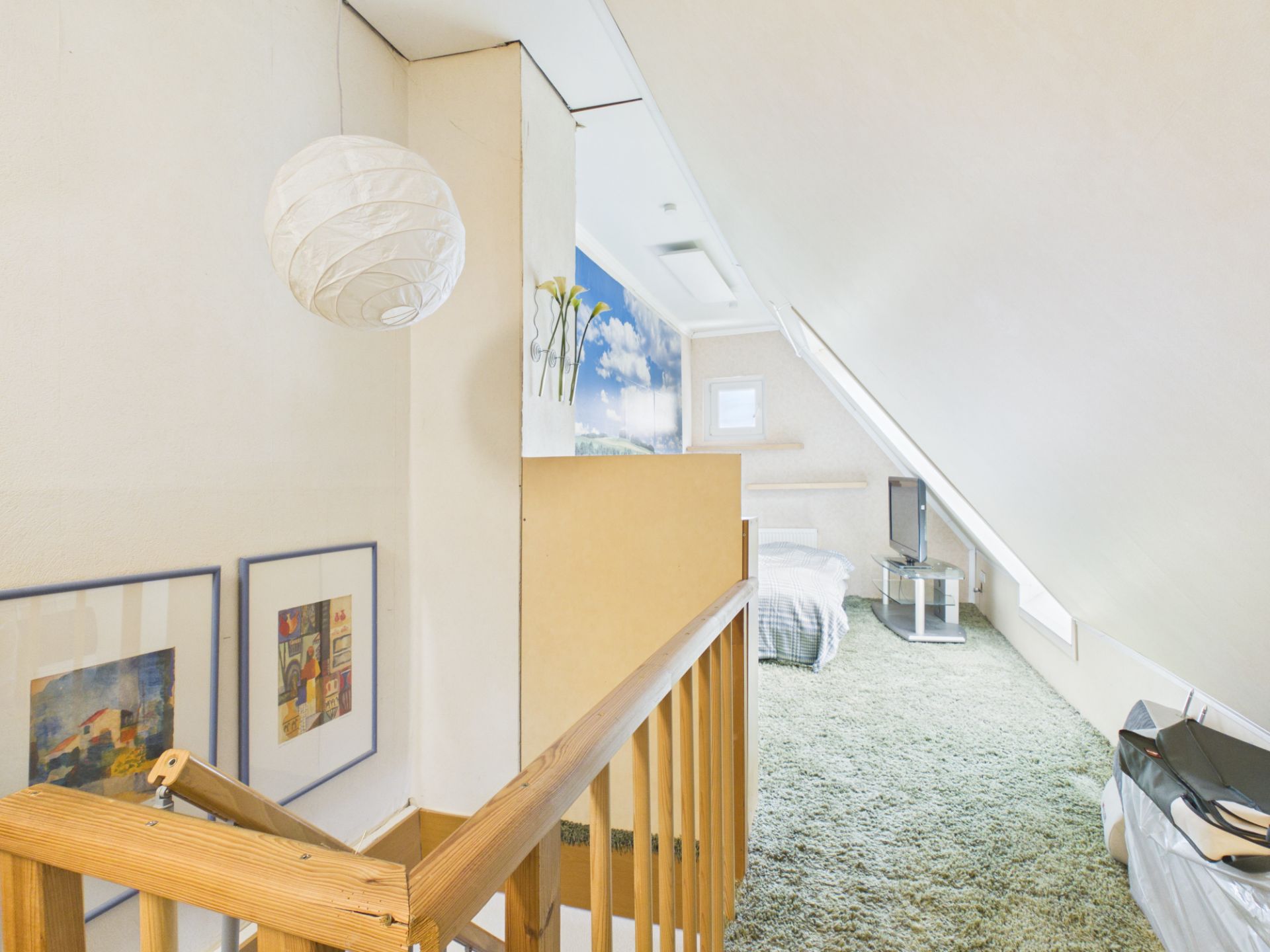 Helles Dachzimmer mit Bett, Teppichboden, TV, schräge Decke und Holzgeländer.