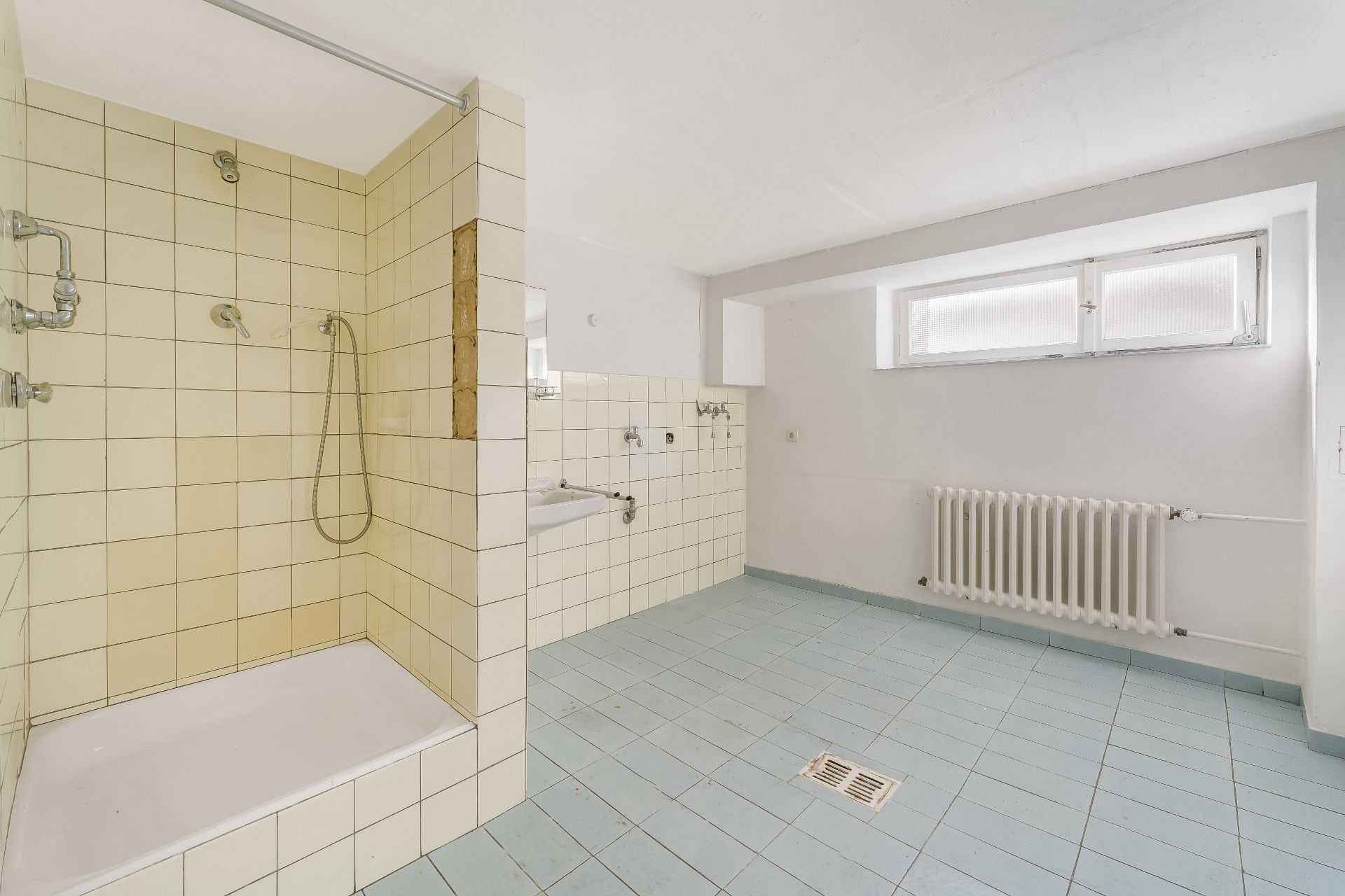 Helles Badezimmer mit begehbarer Dusche, Waschbecken, Fenster und Heizkörper.