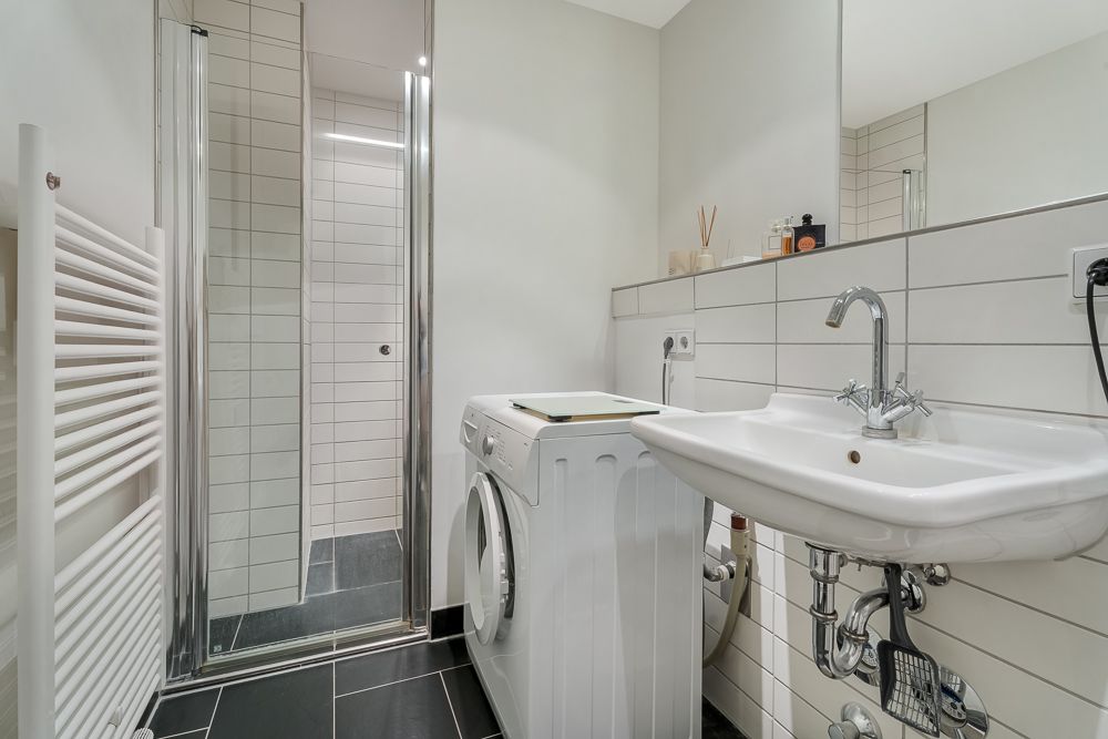 Modernes Badezimmer mit Waschbecken, Waschmaschine, Handtuchheizkörper und Duschkabine.