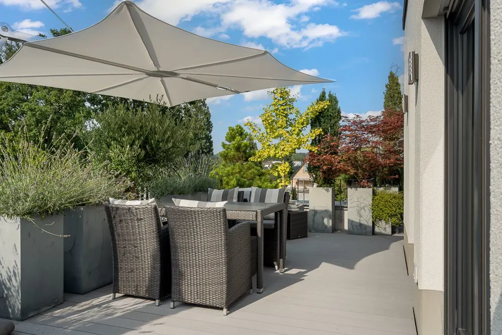 Moderne Terrasse mit Esstisch, Stühlen und großem Sonnenschirm, umgeben von Pflanzen.