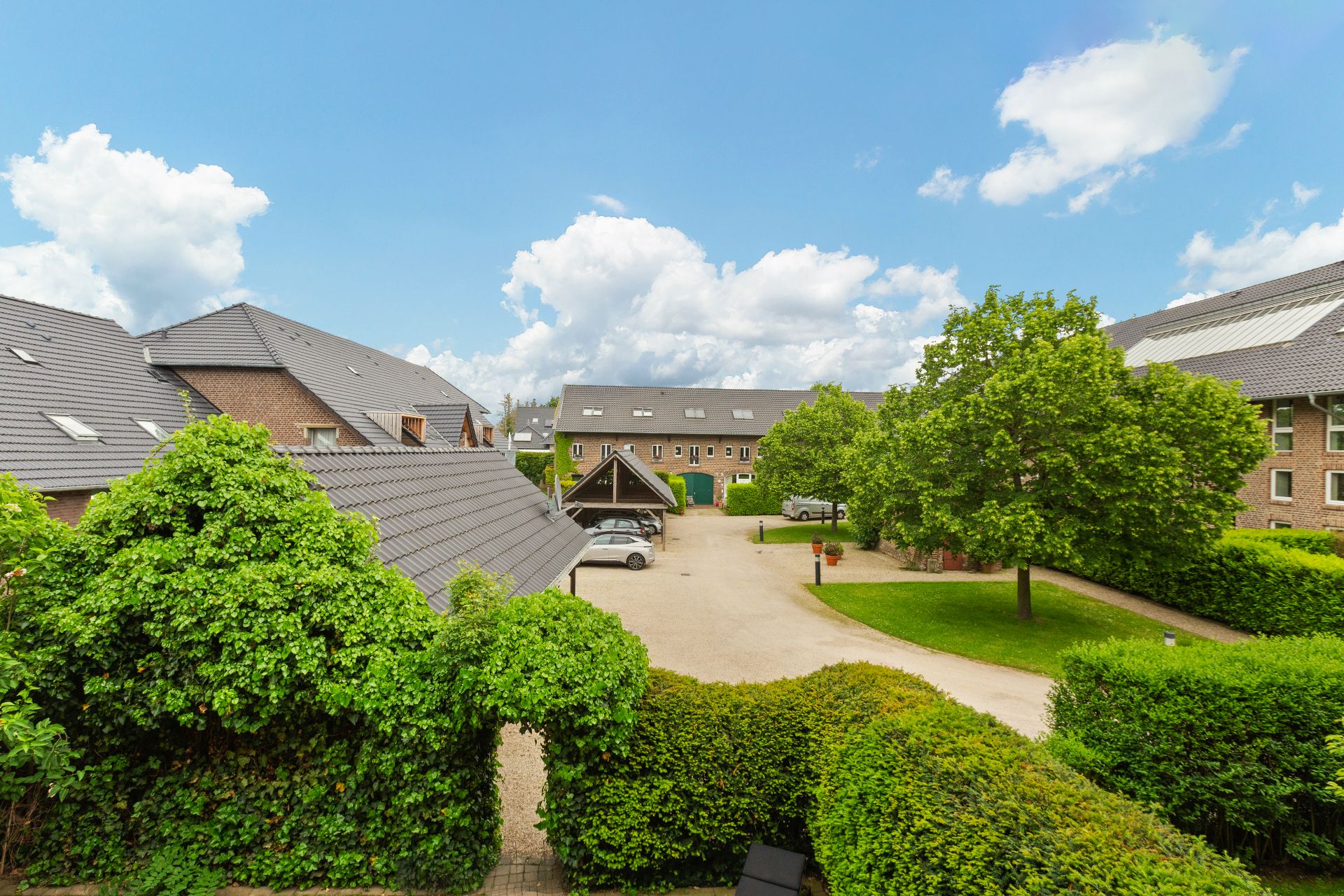 Innenhof mit Parkplätzen, grüner Hecke und Bäumen, umgeben von Wohnhäusern bei sonnigem Wetter.