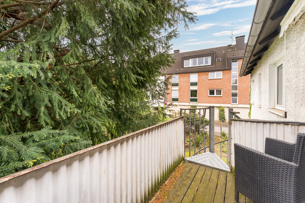 Kleiner Balkon mit Stuhl, Blick auf grünen Baum und Wohngebäude gegenüber.