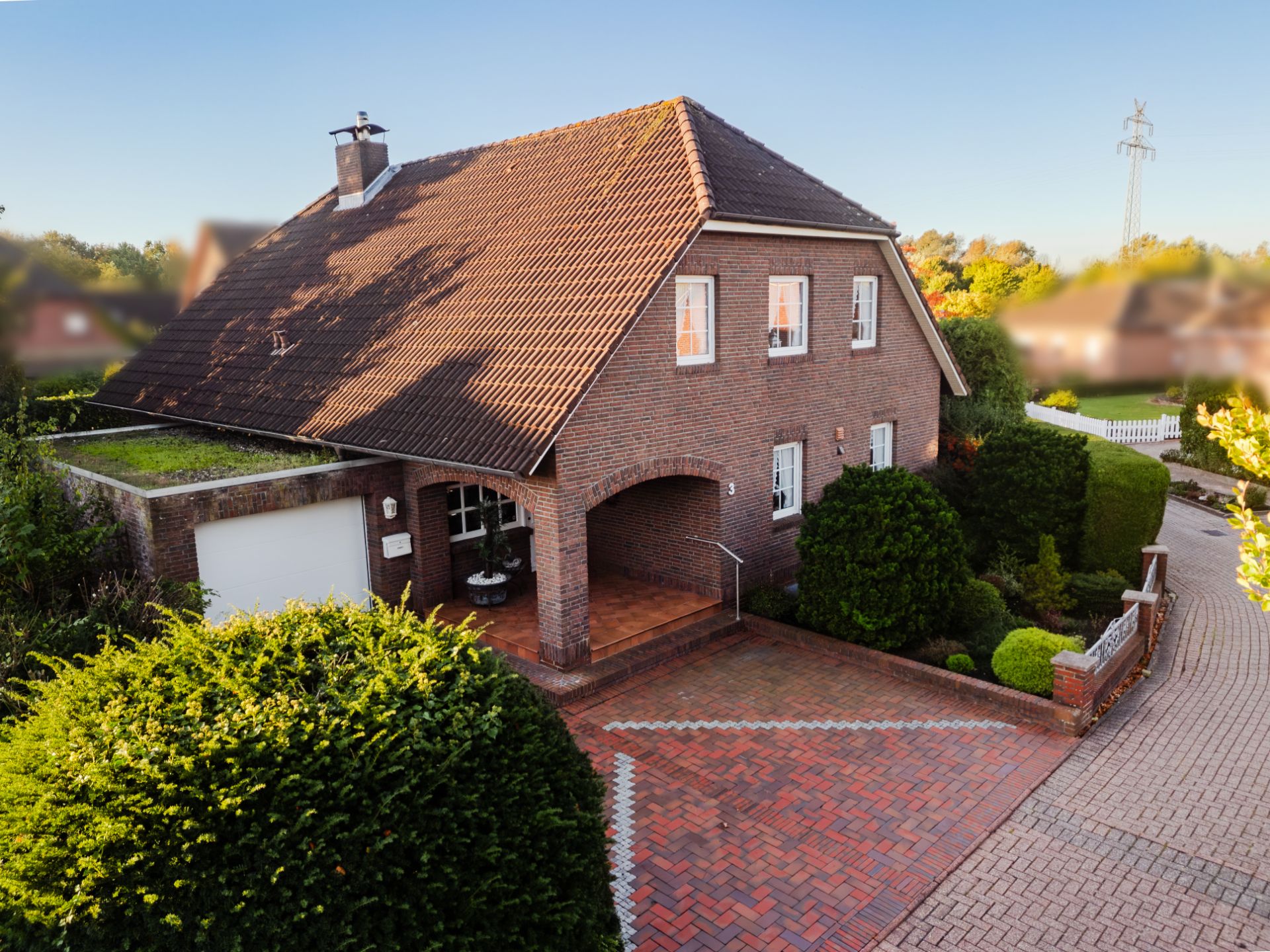 Backsteinhaus mit Satteldach, Terrasse und Garage, umgeben von Garten und gepflasterter Einfahrt.