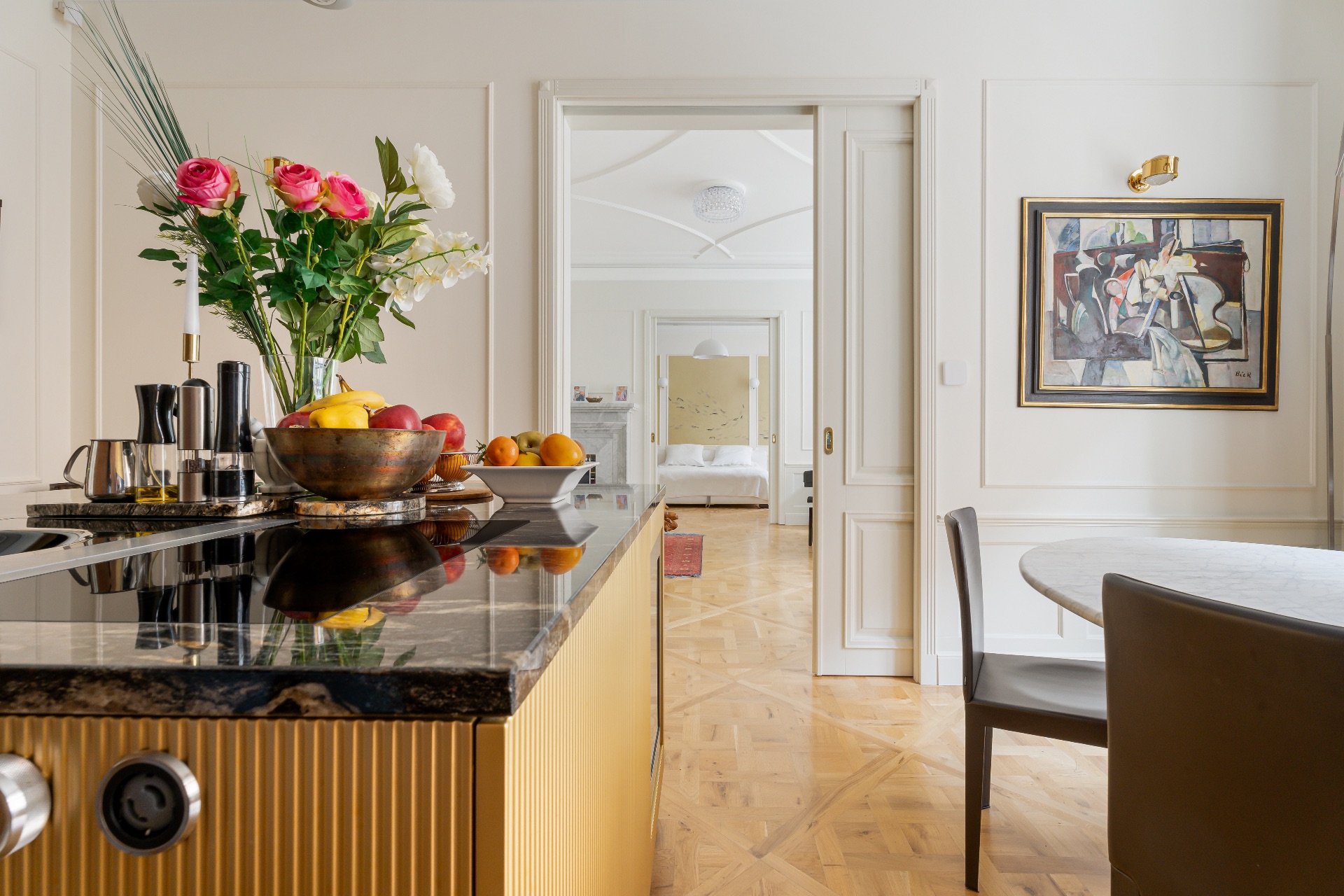 Moderne Küche mit Blumen, Obstschale und Blick in ein helles Schlafzimmer.