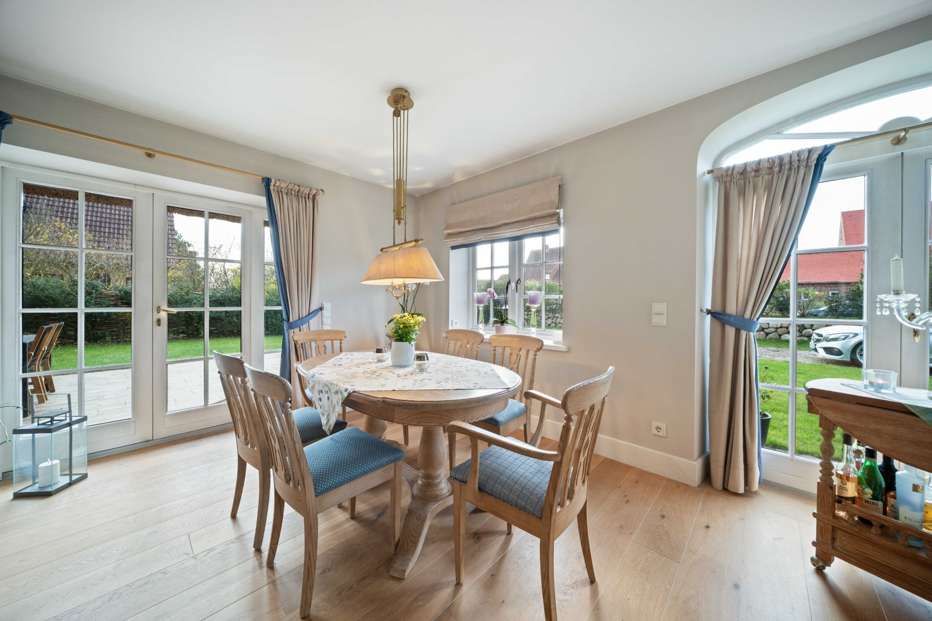 Heller Essbereich mit rundem Holztisch, sechs Stühlen und großen Fenstern mit Blick in den Garten.