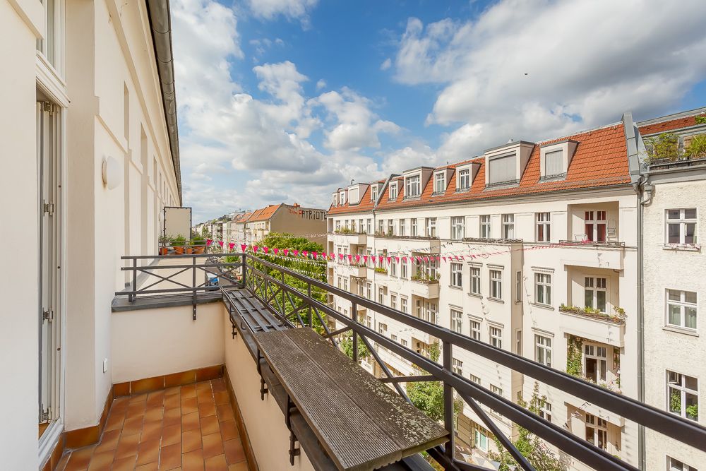 Balkon mit Holzgitter und Blick auf benachbarte Wohnhäuser bei Sonnenschein.