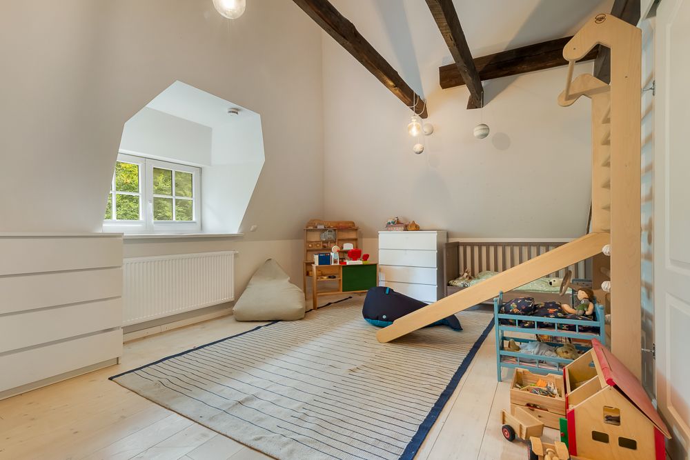 Helles Kinderzimmer mit Spielzeug, Rutsche, Kommoden und Teppich unter schrägem Dach.