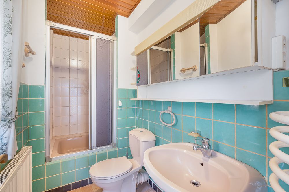 Kleines Badezimmer mit Dusche, WC, Waschbecken und türkisfarbenen Fliesen.