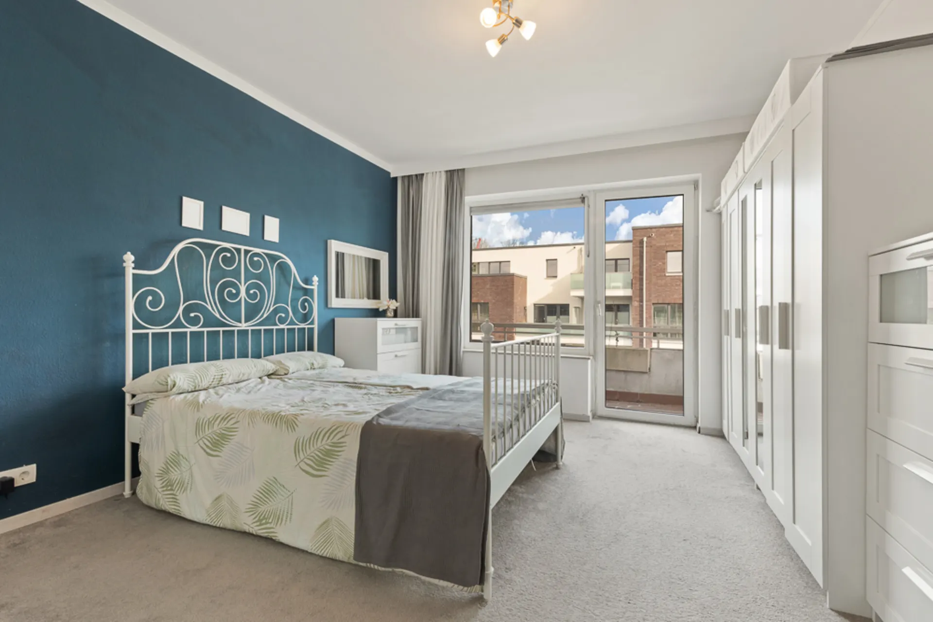 Helles Schlafzimmer mit Doppelbett, weißem Kleiderschrank und Zugang zu einem Balkon.
