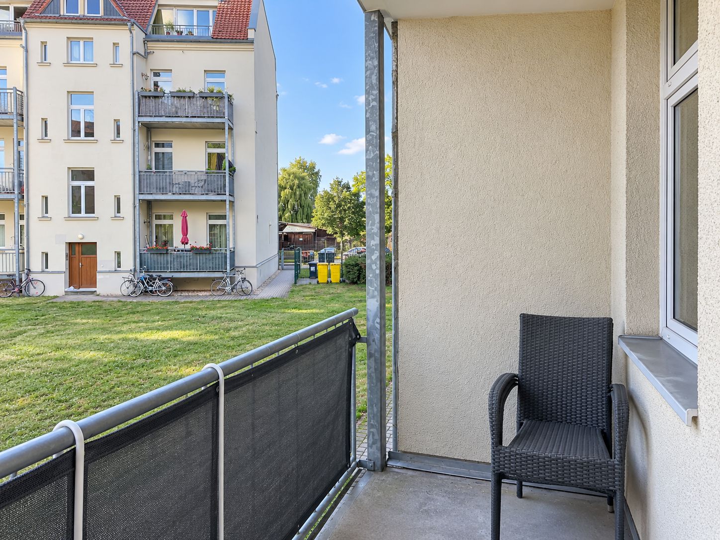 Balkon mit Stuhl und Blick auf eine Wiese sowie ein Mehrfamilienhaus im Hintergrund.