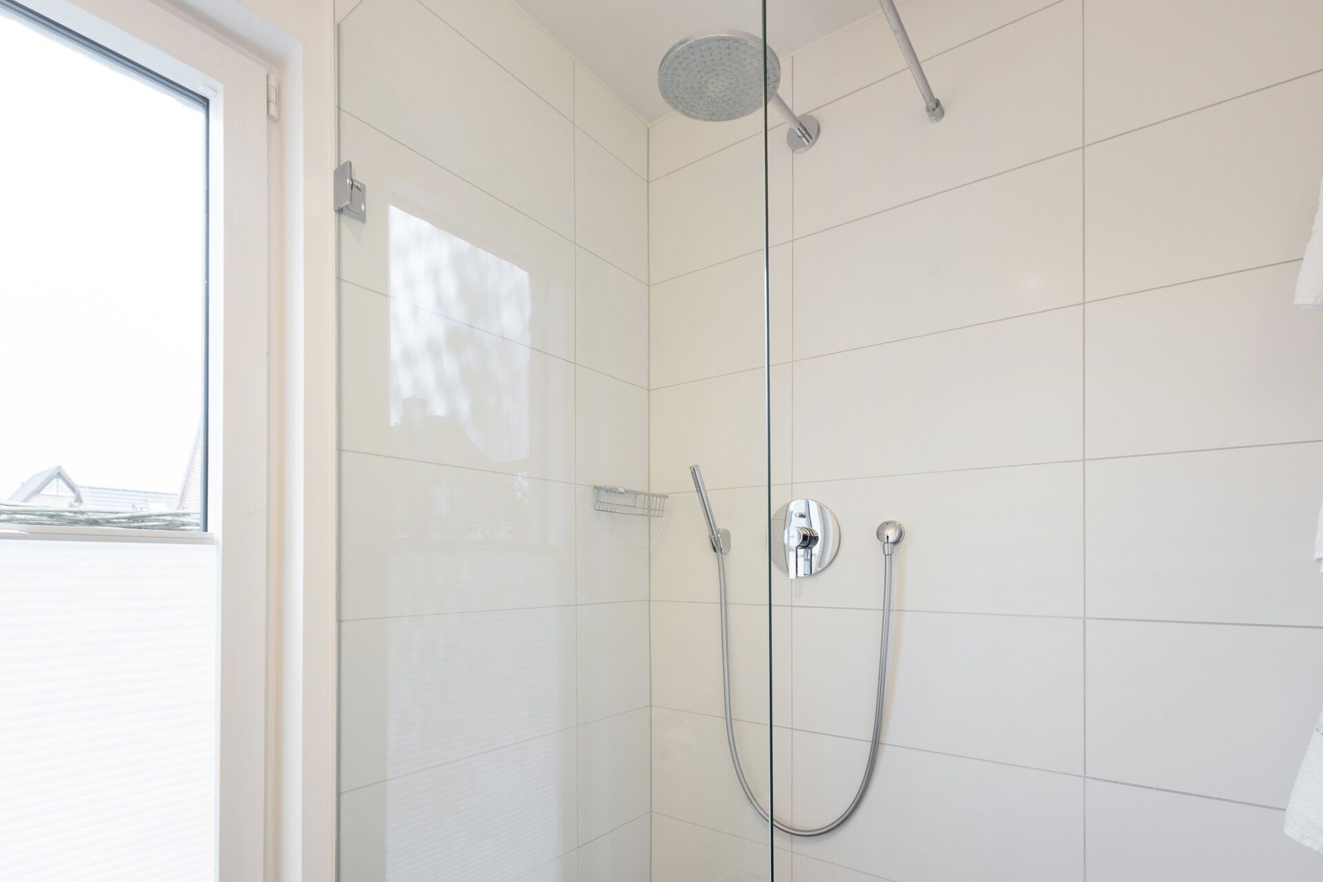 Moderne Dusche mit Glaswand und großem Duschkopf neben einem Fenster.