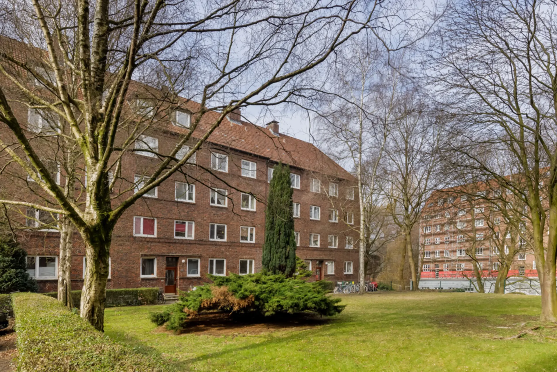 Mehrstöckiges Wohnhaus aus Ziegelstein mit Bäumen und grüner Wiese im Vordergrund.