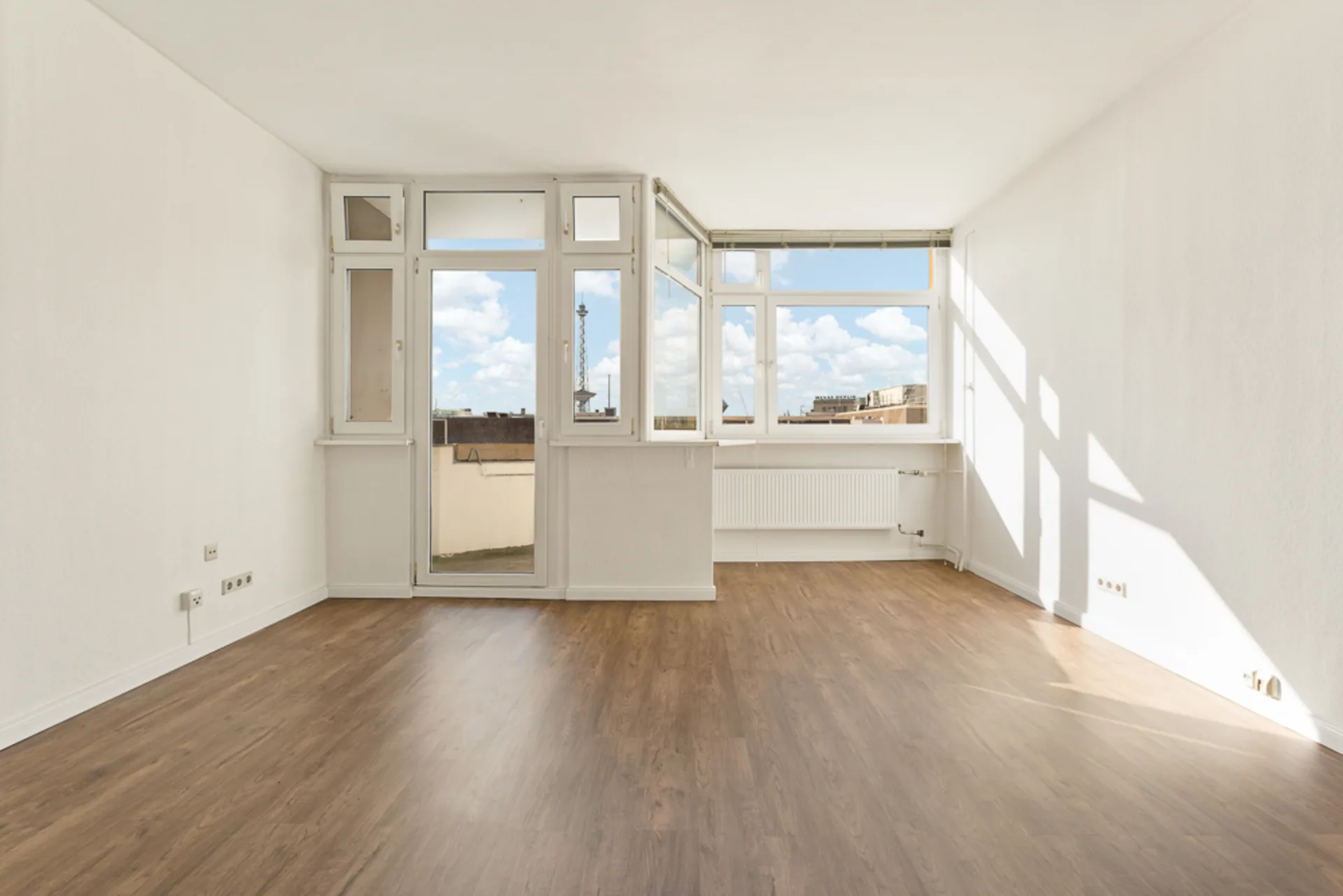 Heller, leerer Raum mit großen Fenstern, weiß gestrichenen Wänden und Holzboden.