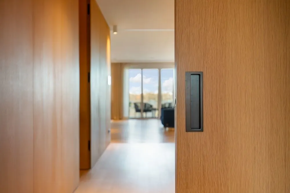 Modernes Wohnzimmer mit Holztüren und großen Fenstern im Hintergrund.