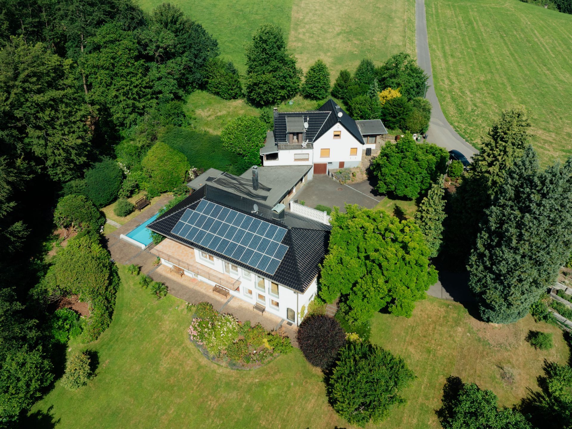 Luftaufnahme eines Hauses mit Solarpanels, Garten und Pool, umgeben von viel Grün.
