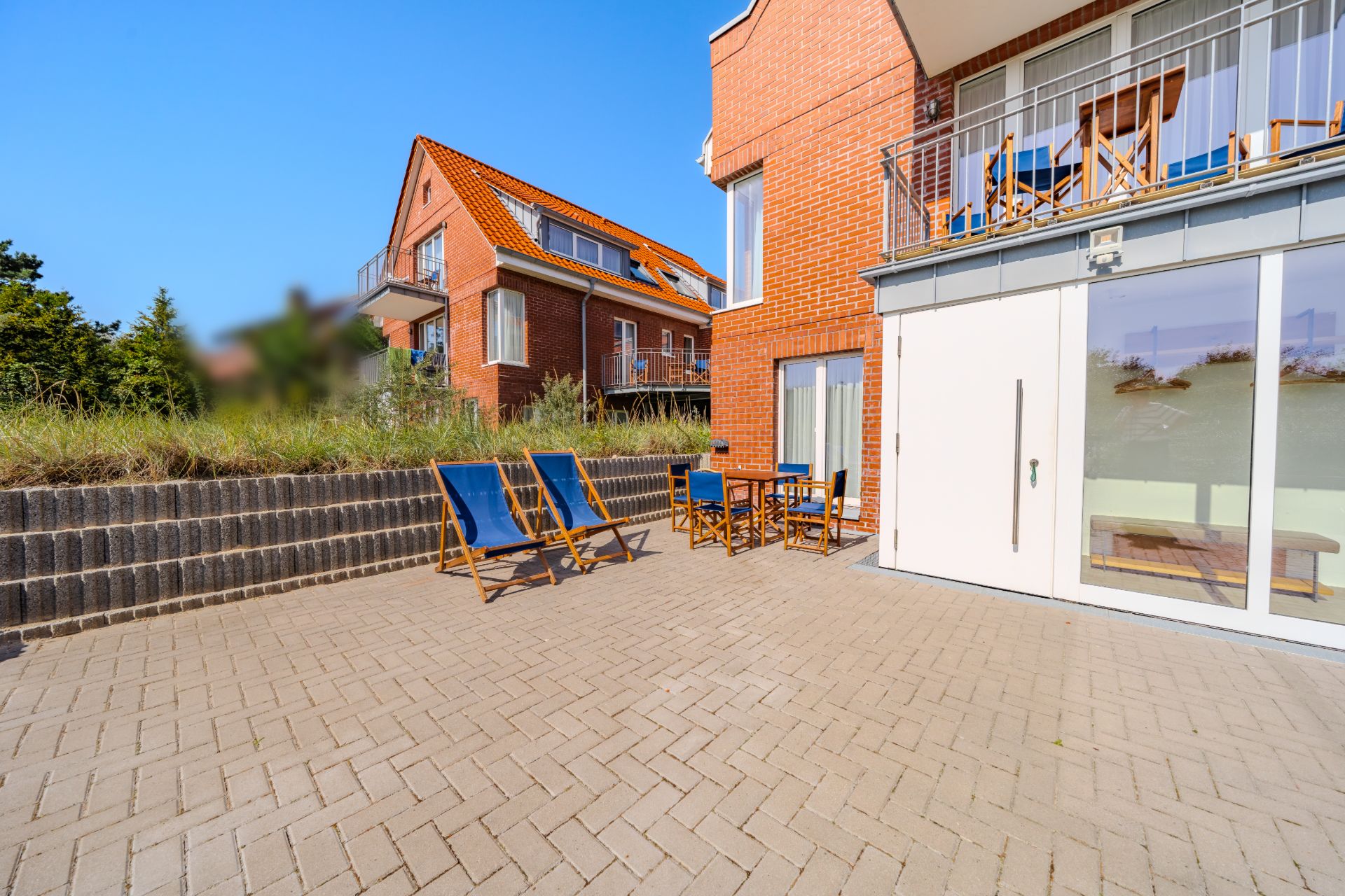 Sonnige Terrasse mit Liegestühlen und Sitzgruppe vor einem Backsteinhaus.